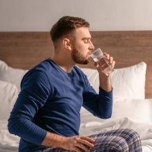 muž sedí na posteli a pije vodu